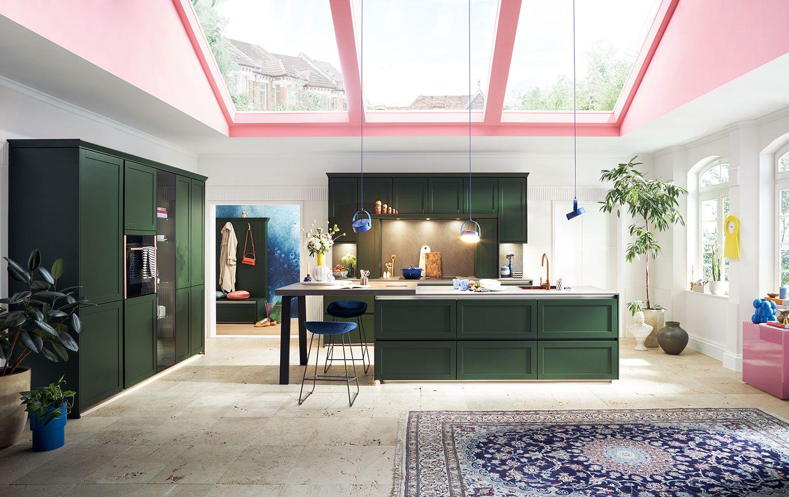 Exklusive Schüller Küche in dunklem Grün mit großer Kochinsel, pinkem Glasdach und elegantem Wohnambiente.