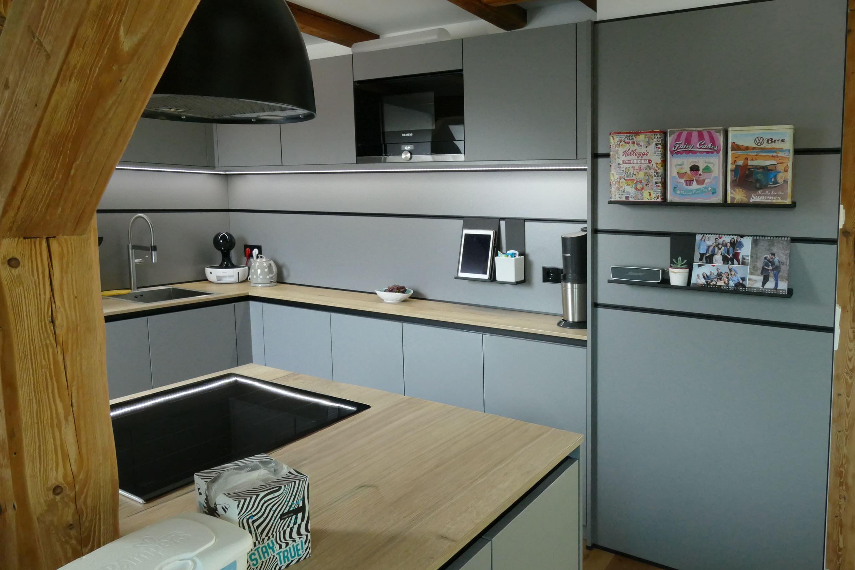 Graue Küche mit Holzarbeitsplatten, klaren Linien und integrierter LED-Lichtleiste, geplant vom Küchenstudio Hölzel Küchen Design.