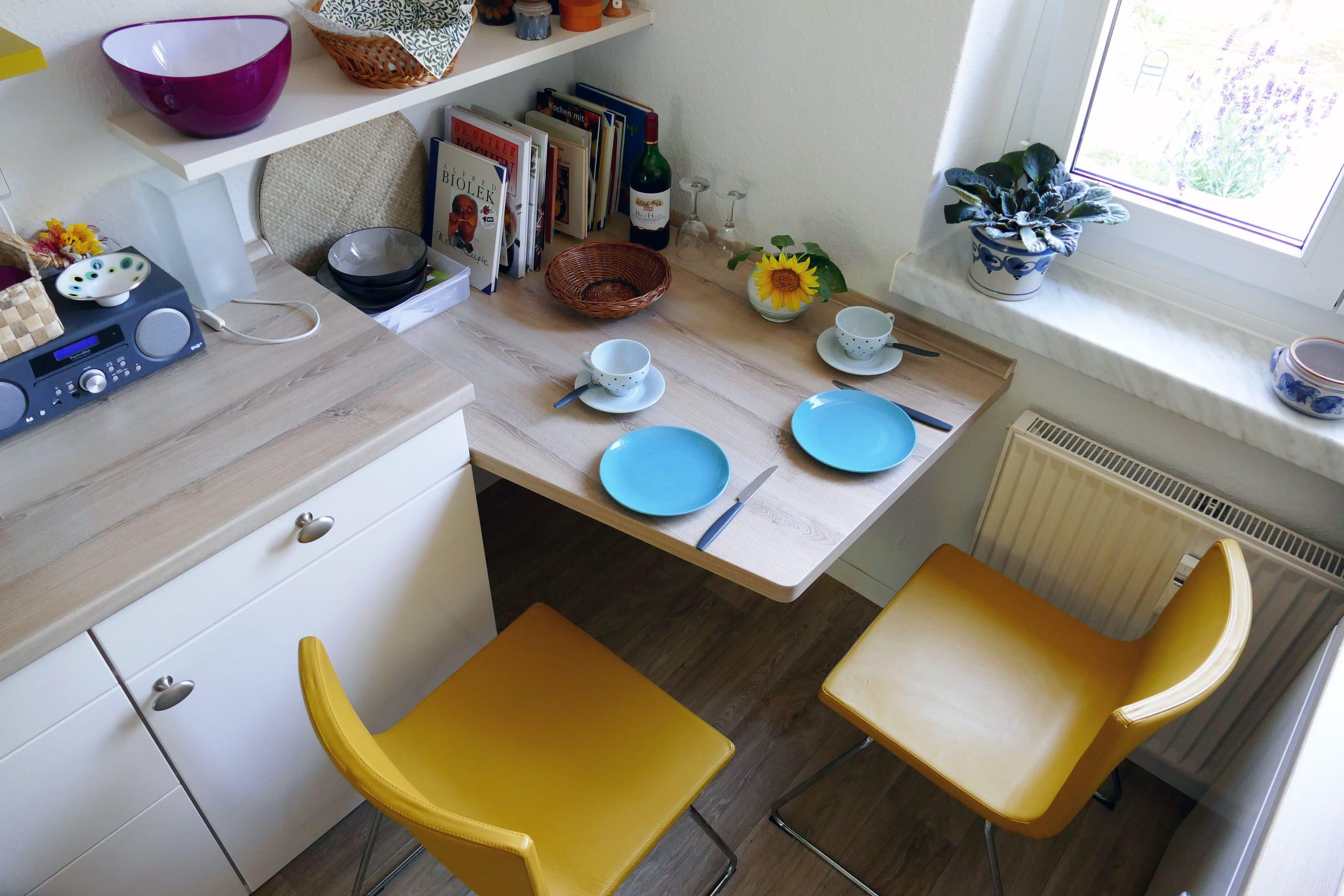 Kleiner Essbereich mit ausziehbarer Holzplatte und zwei gelben Stühlen, geplant vom Küchenstudio Hölzel Küchen Design.