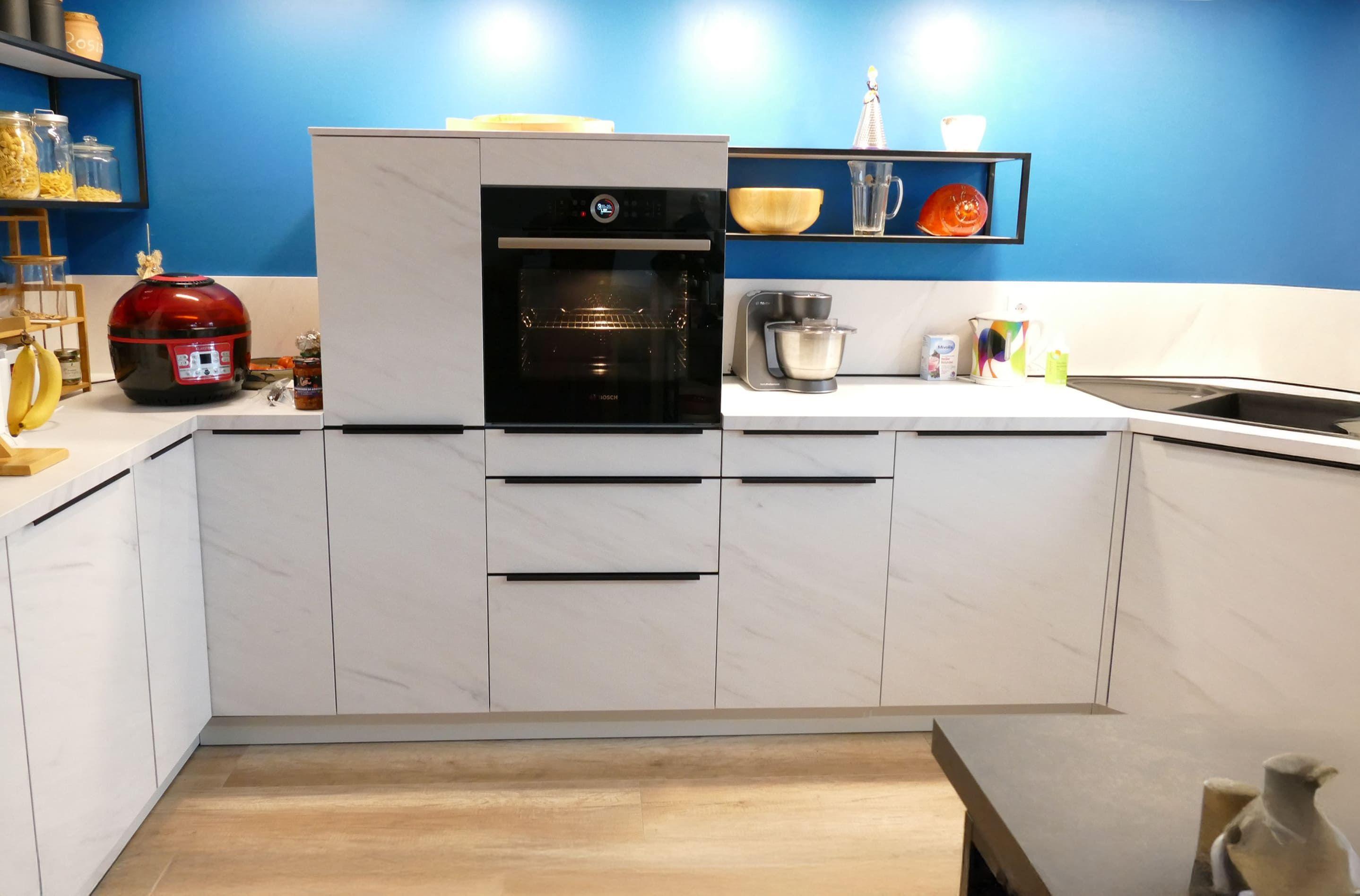 Weiße Küche mit Marmoroptik-Fronten, blauer Rückwand und modernem Backofen, geplant vom Küchenstudio Hölzel Küchen Design.