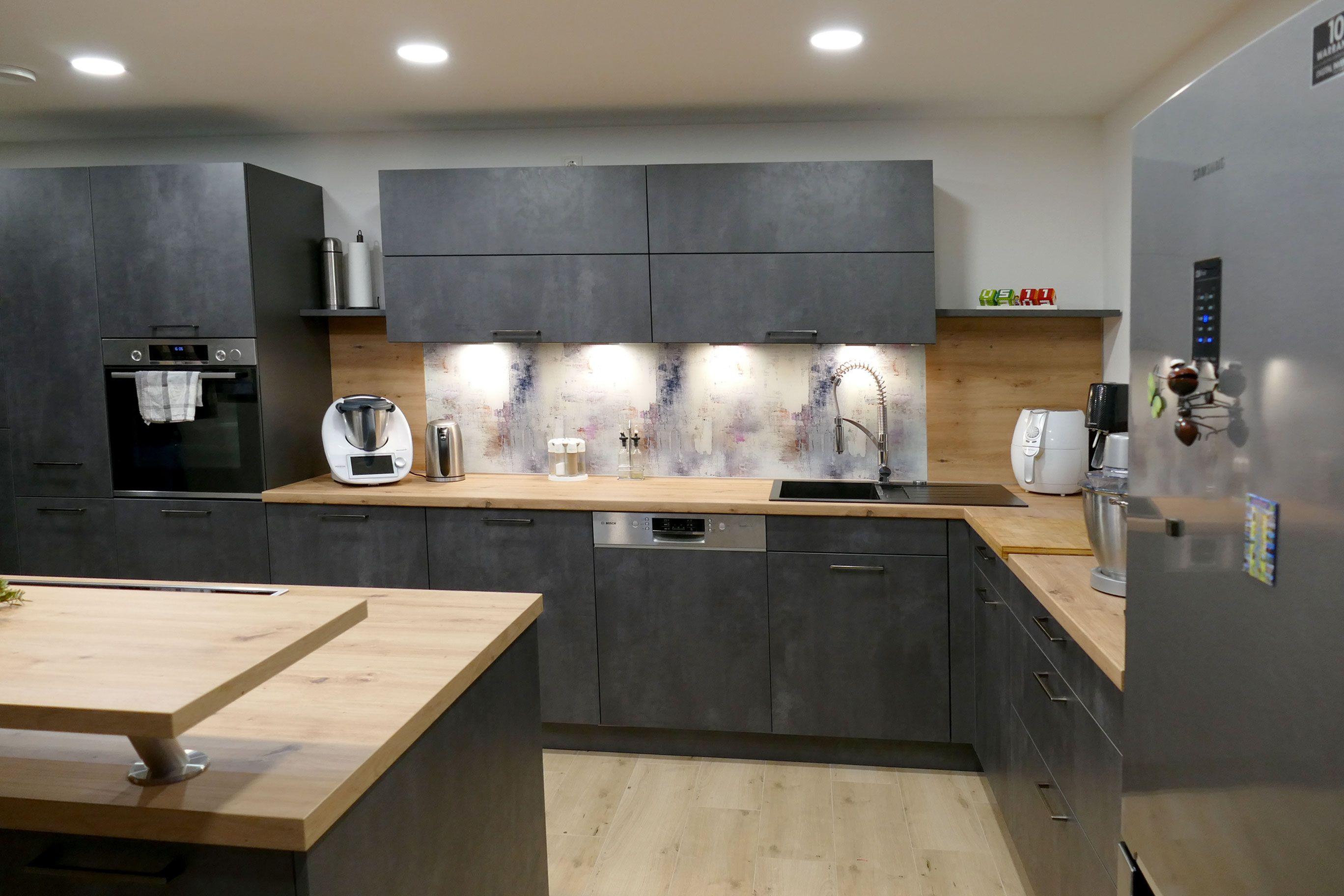 Graue Küche mit Holzdetails, heller Beleuchtung und moderner Geräteausstattung, geplant vom Küchenstudio Hölzel Küchen Design