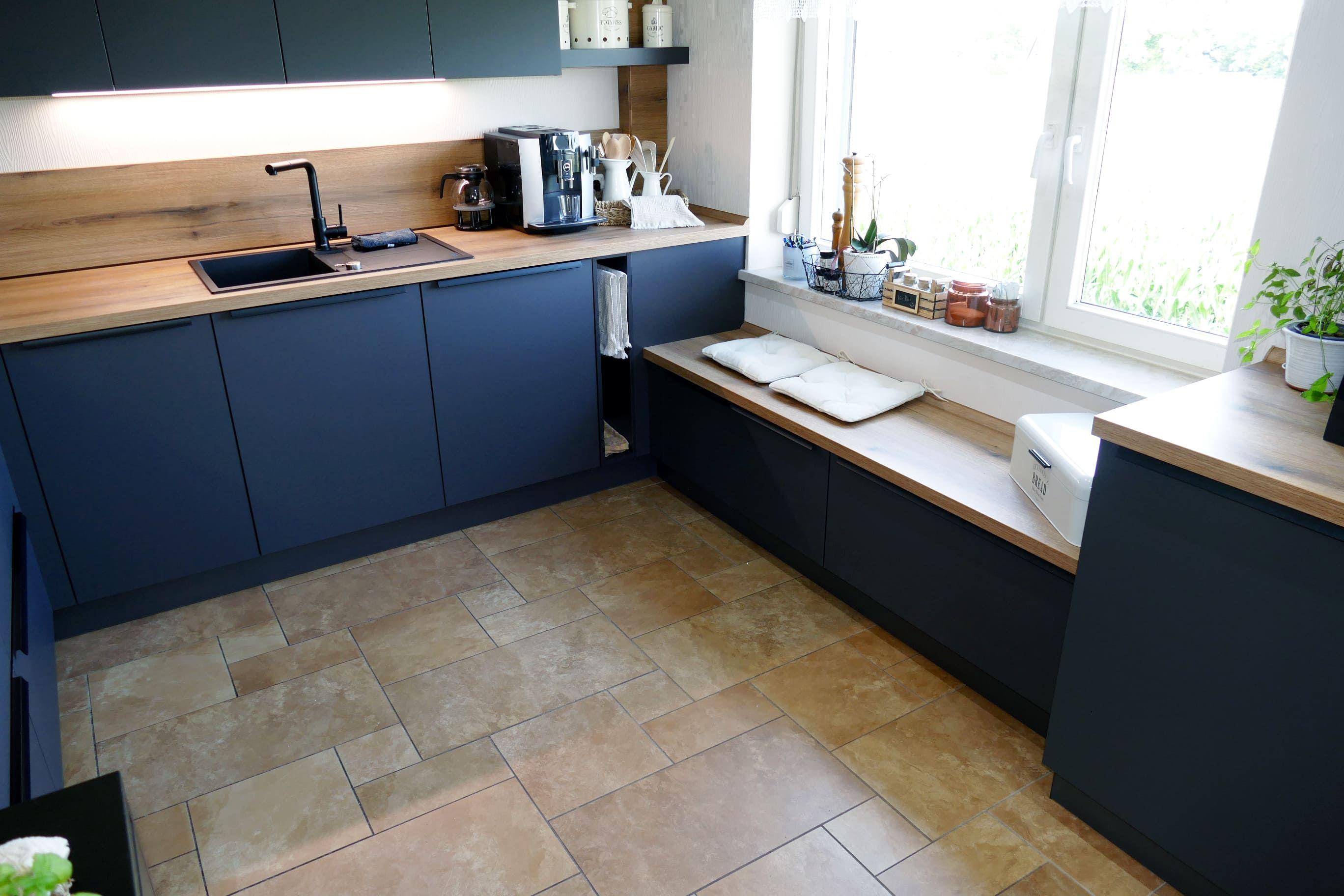 Dunkelblaue Küche mit Holzarbeitsplatten und integrierter Sitzbank am Fenster, geplant vom Küchenstudio Hölzel Küchen Design.